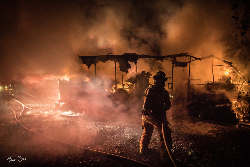 Firefighter standing in front of a burned structure at night